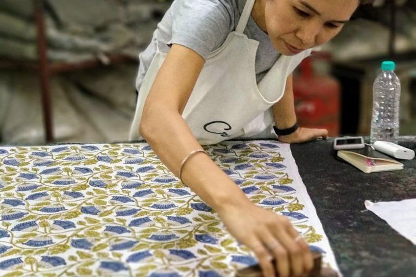 A person working at a table with a patterned tablecloth, a water bottle, and electronic devices. 1