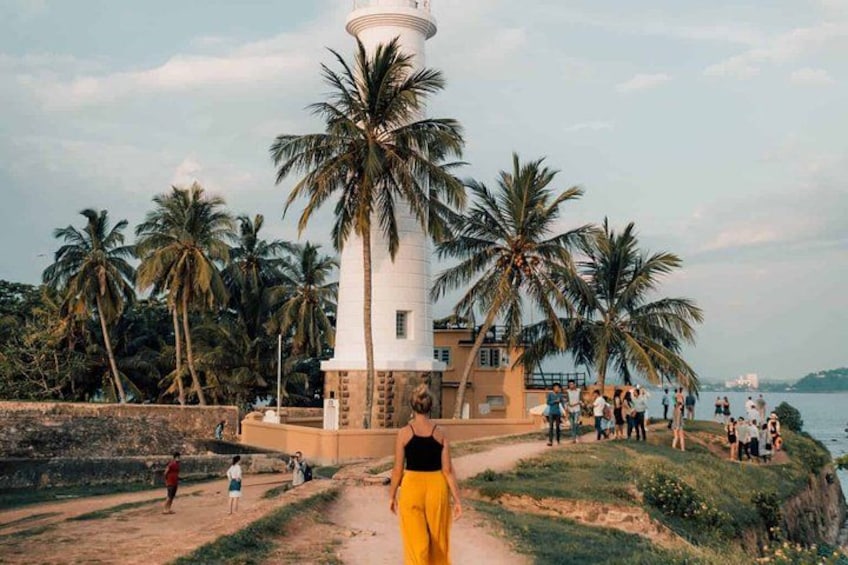 A lighthouse, palm trees, and a beach with people. 1
