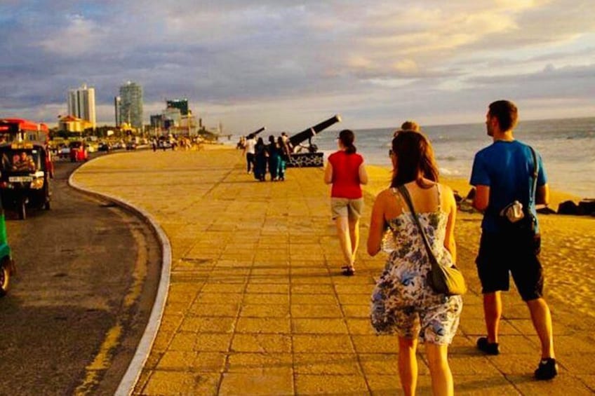 Un paseo marítimo curvo con gente caminando, una calle con vehículos y edificios al fondo. 4