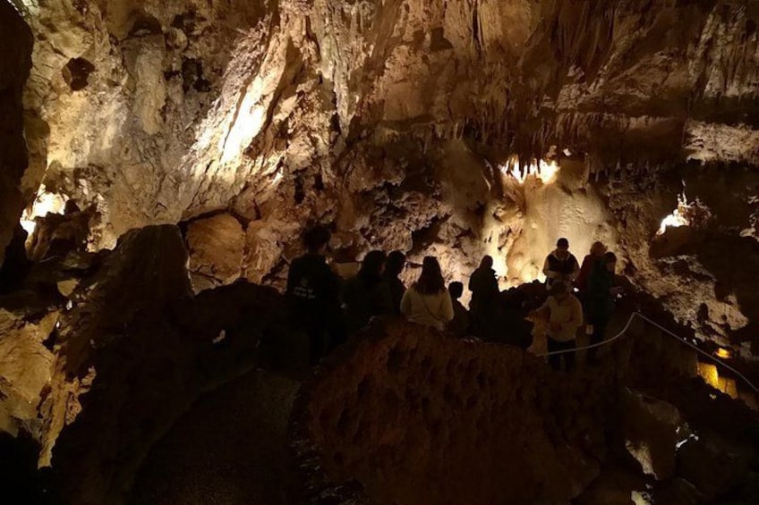 Eine Höhle mit Stalaktiten und Stalagmiten, eine Gruppe von Menschen beobachtet, und eine Seilsperre. 3