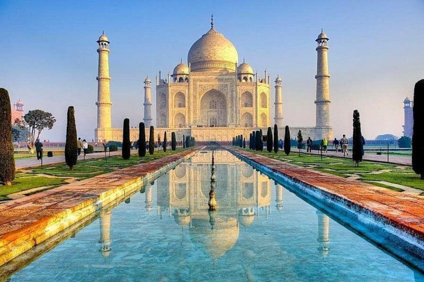 The Taj Mahal with a reflection in the water, surrounded by manicured gardens and minarets. 3