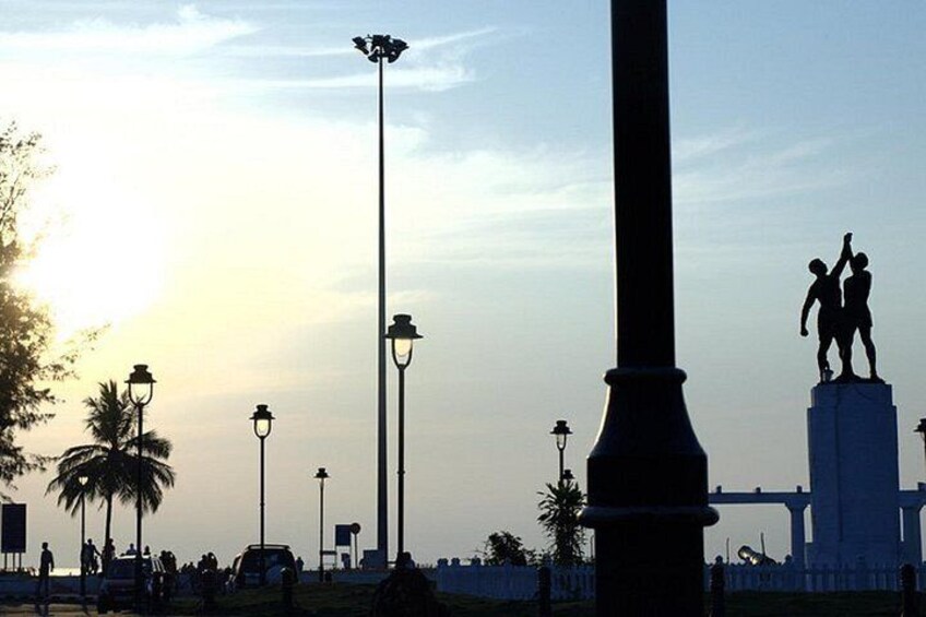 Eine Statue, Straßenlaternen und Palmen bei Sonnenuntergang. 1