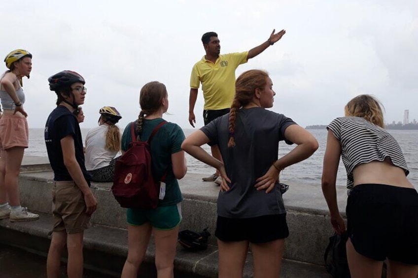 A group of people standing by a waterfront, some wearing helmets and casual clothing. 1