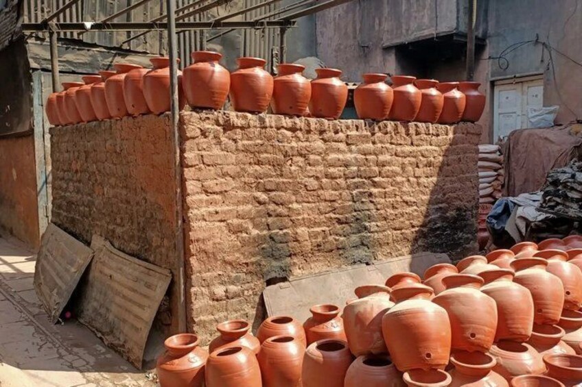 Macetas de terracota apiladas contra un muro de ladrillo, con más macetas dispersas en el suelo. 5