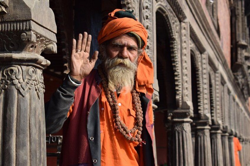 A person in traditional attire with a turban and beaded necklace, standing in front of a building with ornate columns. 4