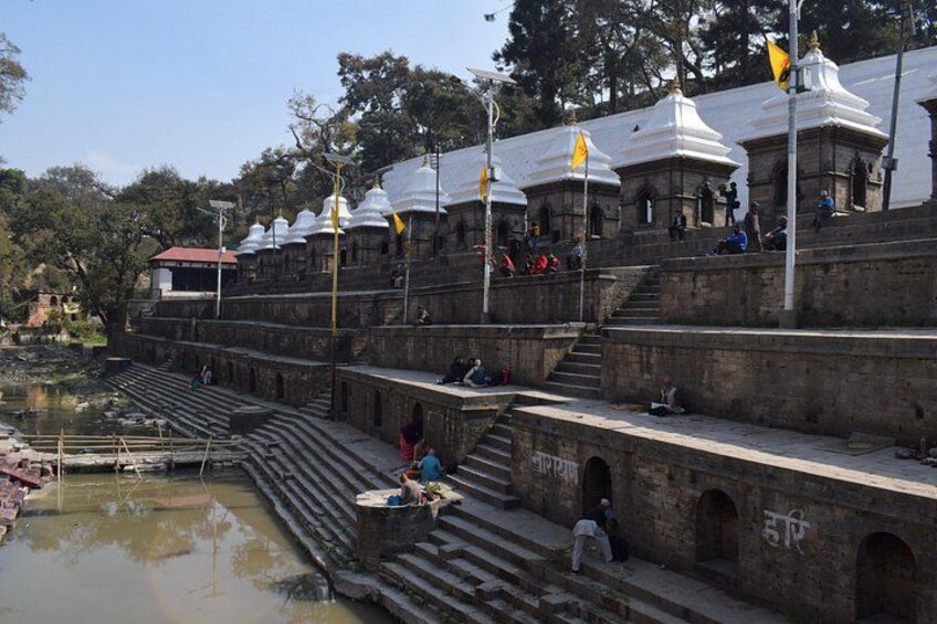 A temple complex with steps leading down to a water body, surrounded by trees and flags. 5
