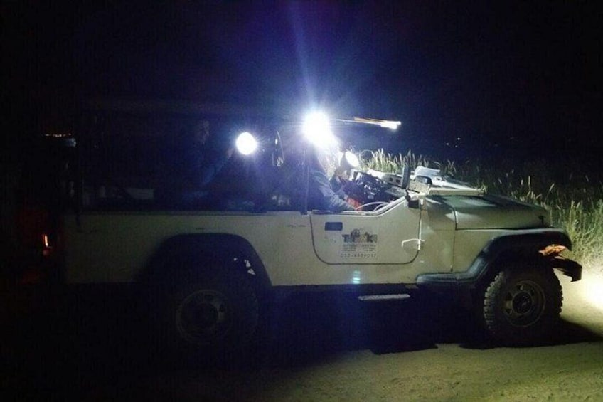 A white off-road vehicle with headlights on, parked on a dirt road at night. 3