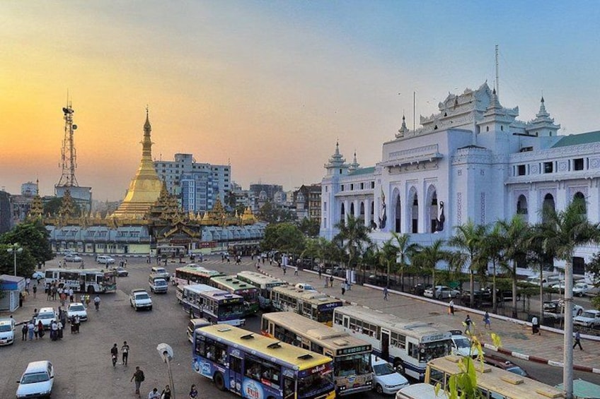 A busy urban street with buses, cars, and pedestrians. A prominent golden stupa and a white colonial-style building are visible. 1