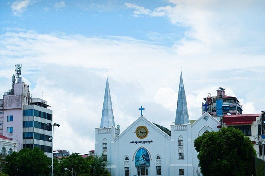A white church with two spires and a clock, surrounded by buildings and trees. 3