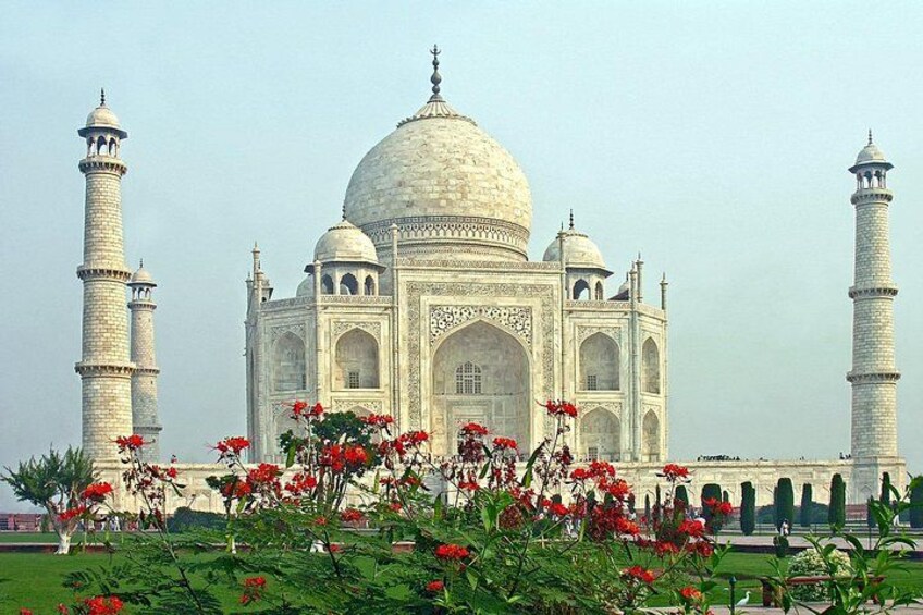 The Taj Mahal with four minarets and a large central dome, surrounded by a garden with red flowers. 1