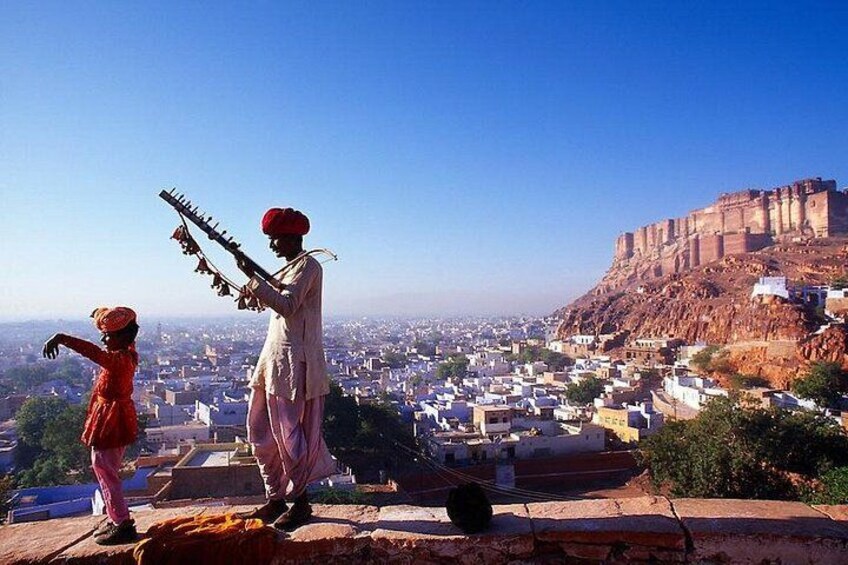 A person playing a traditional stringed instrument, a historic fort in the background, and a cityscape. 4