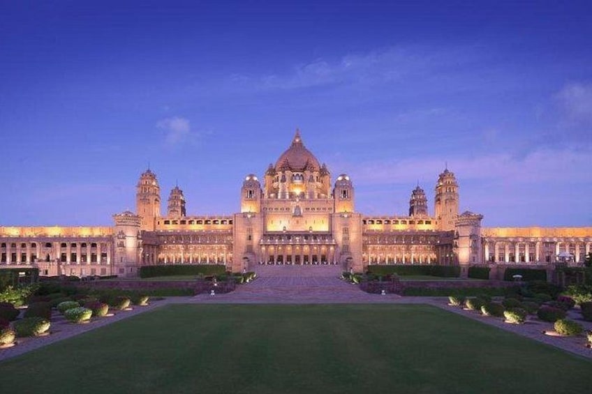 A grand, illuminated building with a central dome and symmetrical wings, surrounded by a well-maintained lawn and pathways. 2