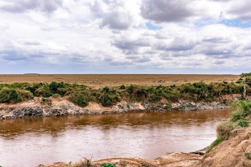 A river with a dry riverbed, sparse vegetation, and a cloudy sky. 4