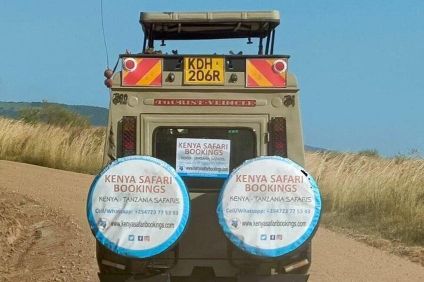 A safari vehicle with 'KENYA SAFARI BOOKINGS' on the back and two circular signs with the same text. 1