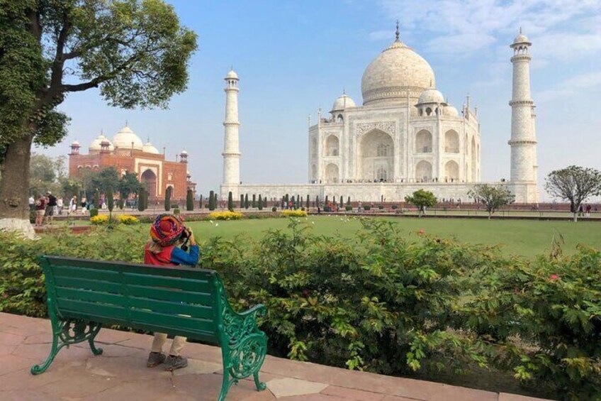 The Taj Mahal with a green bench and a person sitting on it. 1