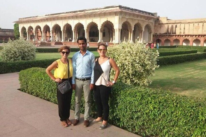 Three people standing in front of a historic building with arches and a well-maintained garden. 5