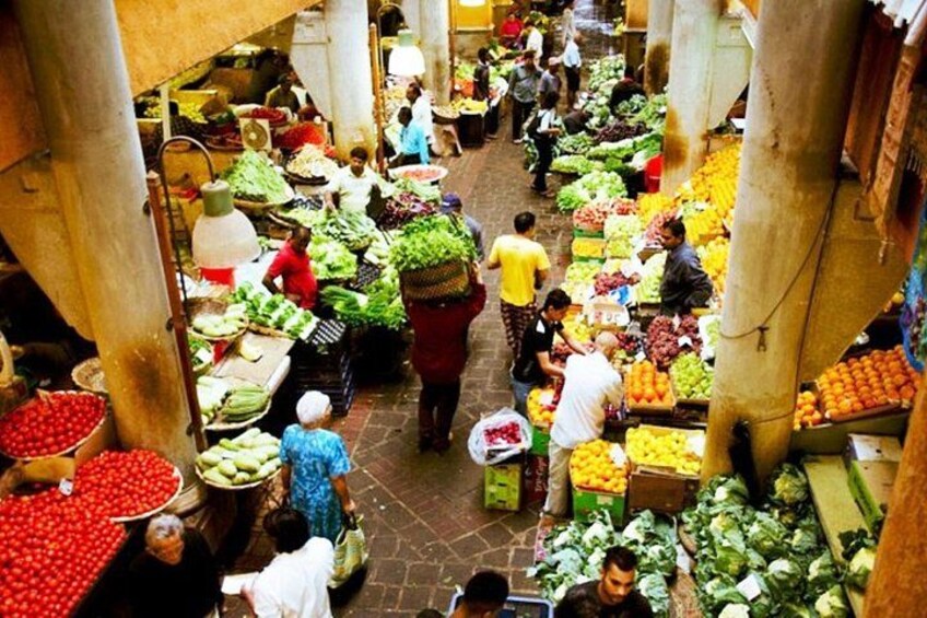 A bustling indoor market with various stalls selling fruits and vegetables. 1