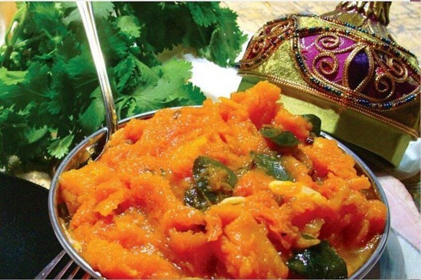 A bowl of orange-colored food with green vegetables, a spoon, and a decorative bag. 3