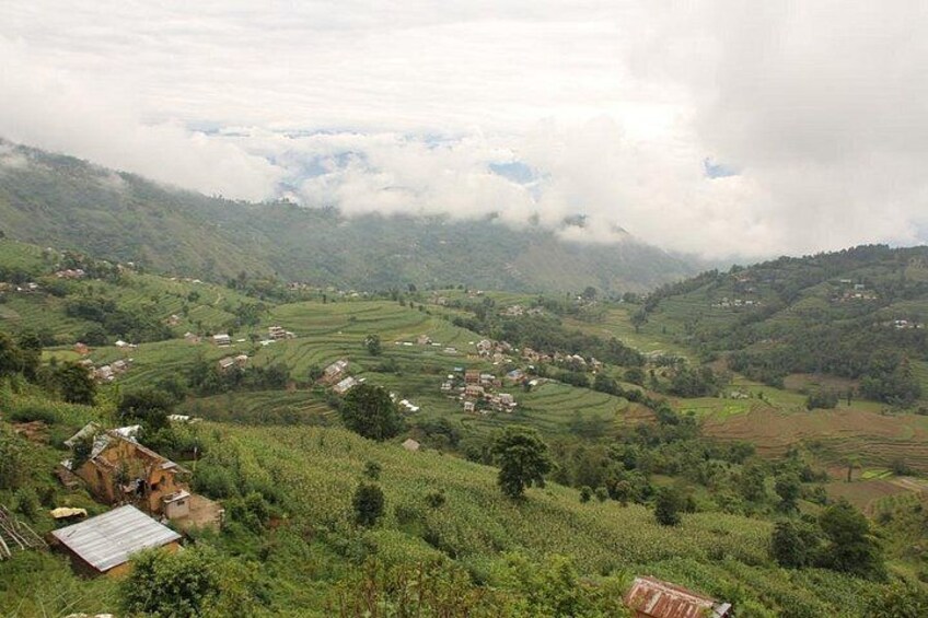 A hilly landscape with terraced fields, scattered houses, and a cloudy sky. 2