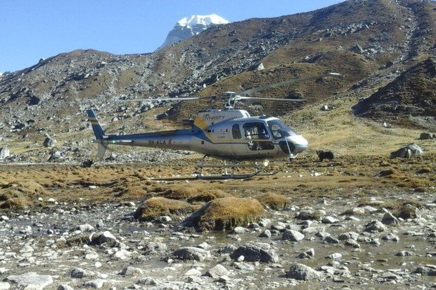 Un hélicoptère est garé sur un terrain rocailleux, avec une chaîne de montagnes en arrière-plan. 2