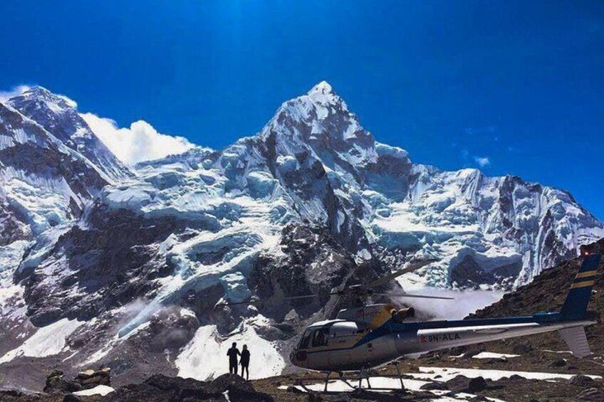 Un hélicoptère sur une montagne enneigée, avec deux personnes debout à proximité. 1