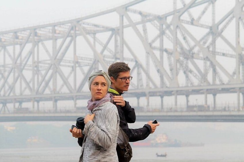 A person carrying another person across a body of water with a large bridge in the background. 2