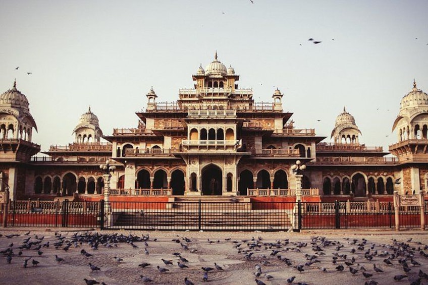 A historic building with domes and arches, surrounded by a large number of pigeons. 2