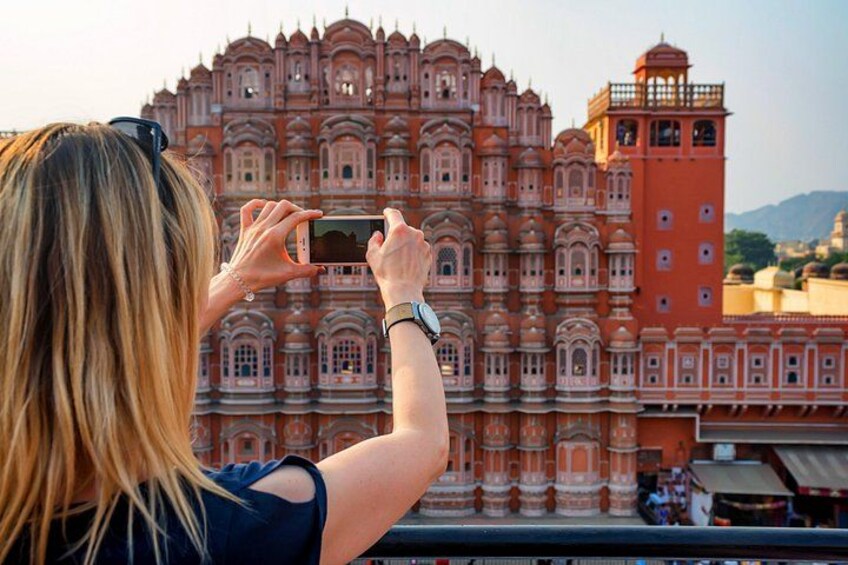 A person taking a photo of a large, ornate building with multiple levels and intricate architectural details. 3