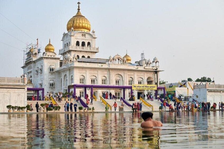 A large white building with golden domes, a reflection pool, and people walking around. 3