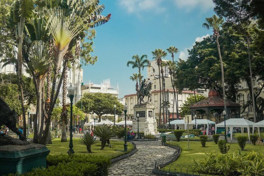 Un parque con una estatua, palmeras, una fuente y un camino adoquinado. 3
