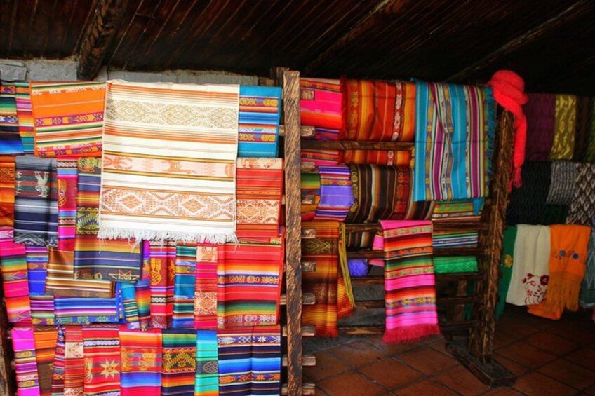 A variety of colorful textiles displayed on wooden racks in a rustic setting. 2