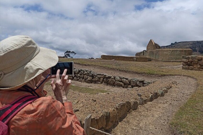 A person taking a photo of ancient ruins with stone walls and a stone pathway. 2