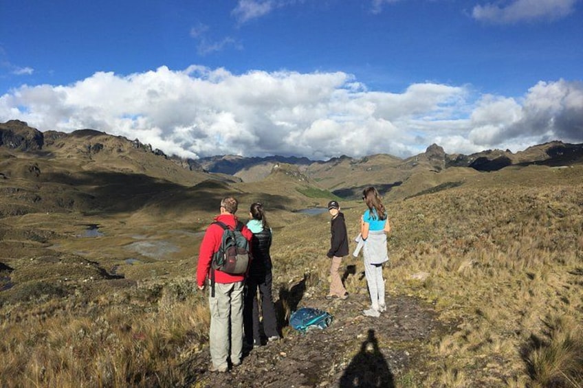 A group of hikers on a mountain trail with a view of a valley and distant mountains. 1