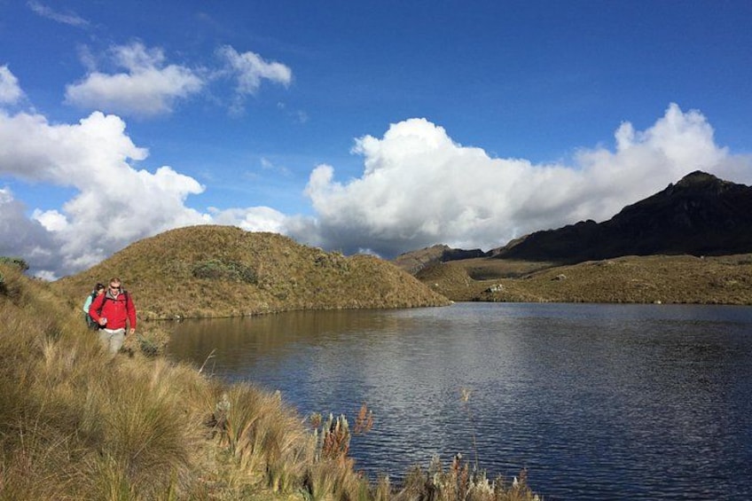A lake surrounded by hills, a person in a red jacket, and a clear blue sky with clouds. 4
