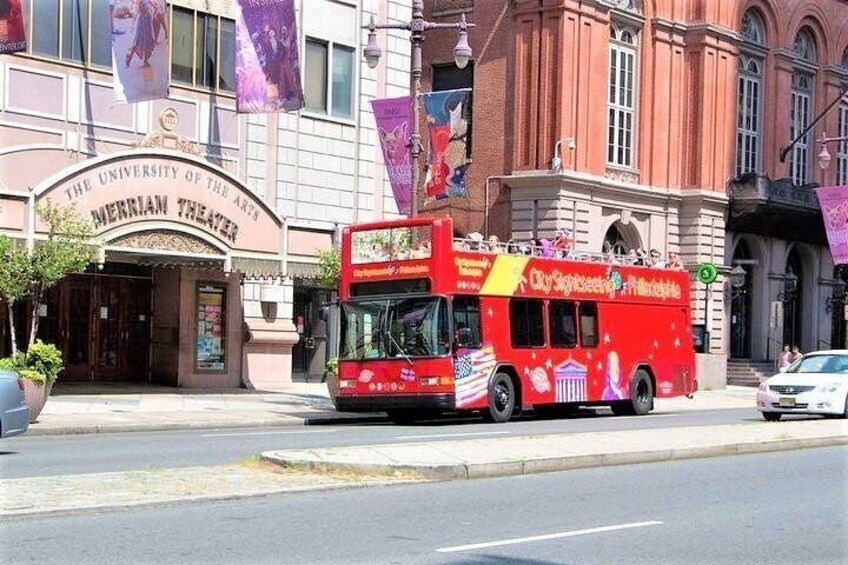 A red double-decker bus with 'City Sightseeing Philadelphia' written on it, parked on a street in front of the University of the Arts Merriam Theater. 4