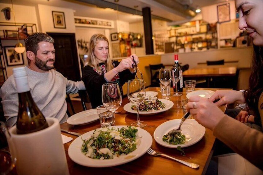 En gruppe mennesker spiser middag på en restaurant med vinglas og tallerkener med mad. 2