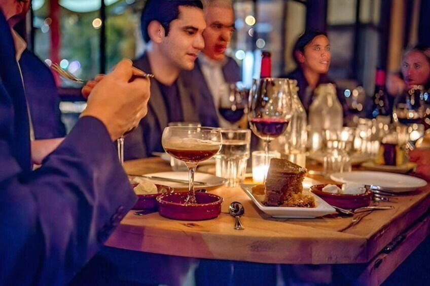 En gruppe mennesker spiser middag på en restaurant med vinglas og tallerkener med mad. 3