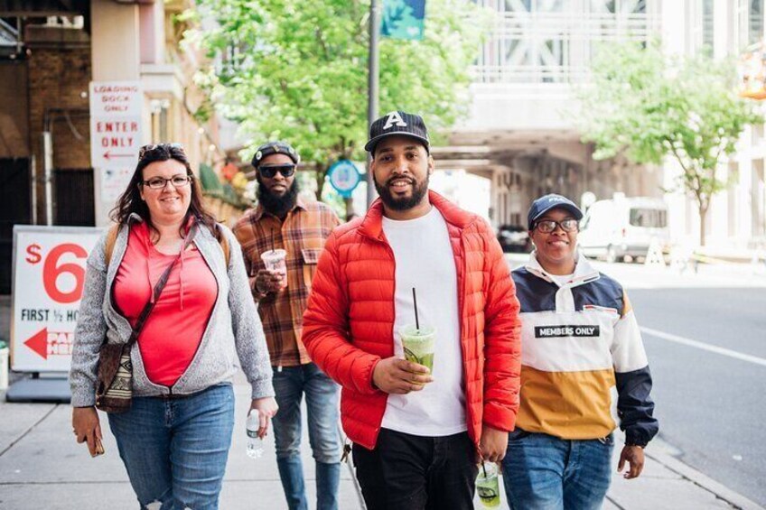 A group of people walking on a city street with a sign indicating a $6 first half price. 1