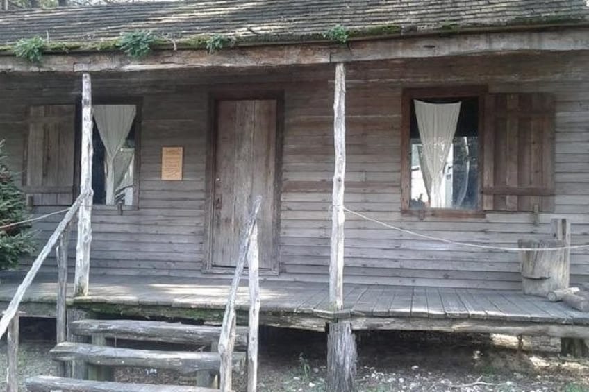Una cabaña rústica de madera con un porche, un ventanal con cortinas y una escalera de madera que lleva a la entrada. 3