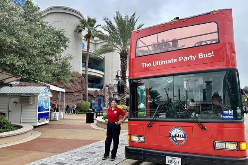 A red double-decker bus with 'The Ultimate Party Bus!' text, parked in a landscaped area with palm trees and a building in the background. 2