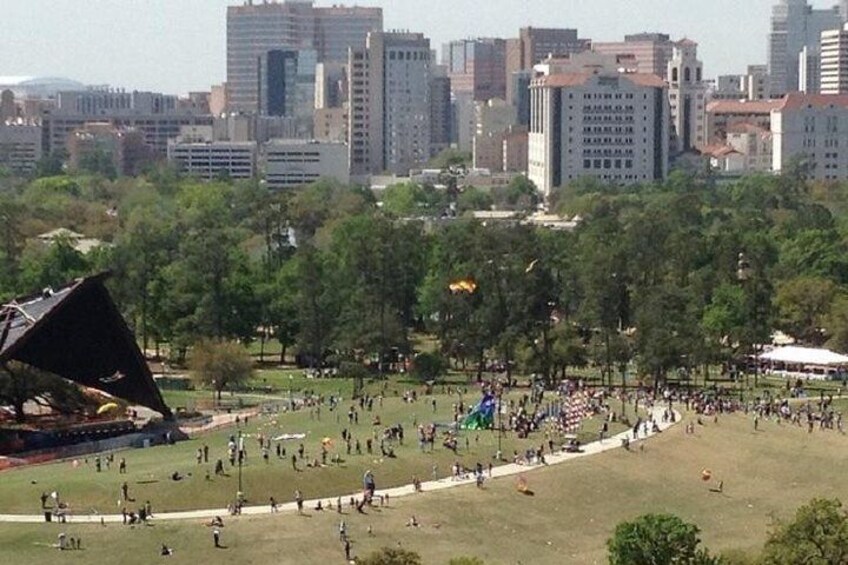 Un parque grande y abierto con gente caminando y sentada sobre el césped, rodeado de árboles y edificios al fondo. 5