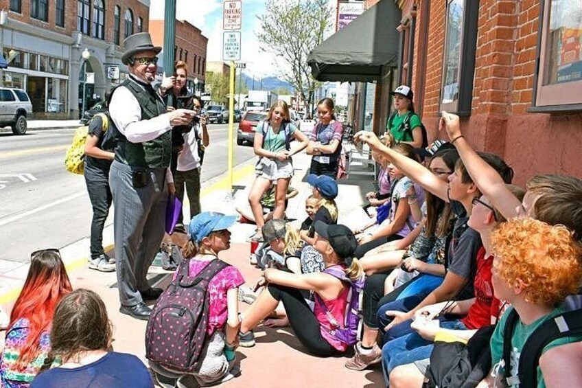 A group of people sitting on the sidewalk, some facing a speaker. 3