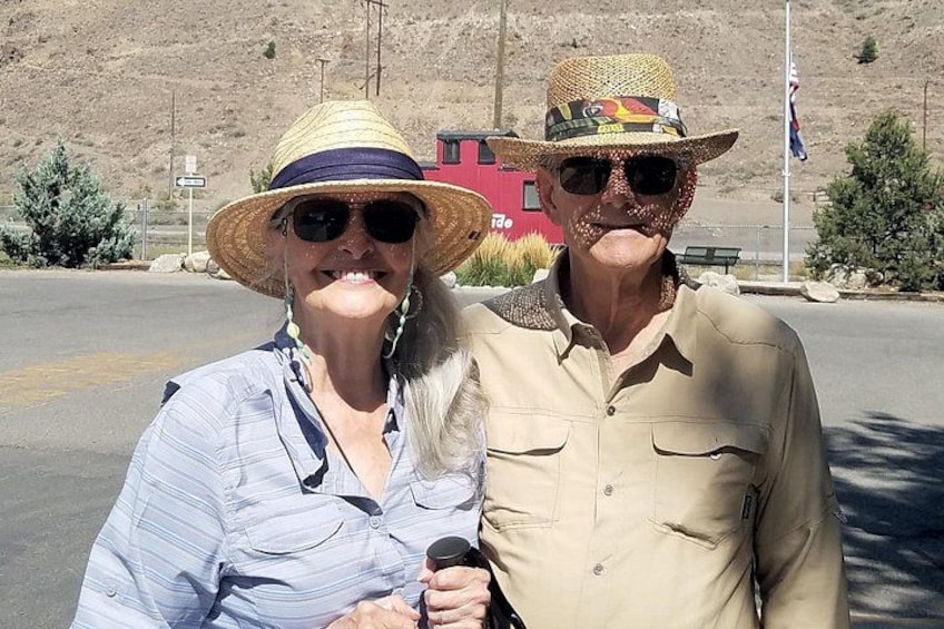 Two people wearing hats and sunglasses, standing on a road with a mountainous background. 2
