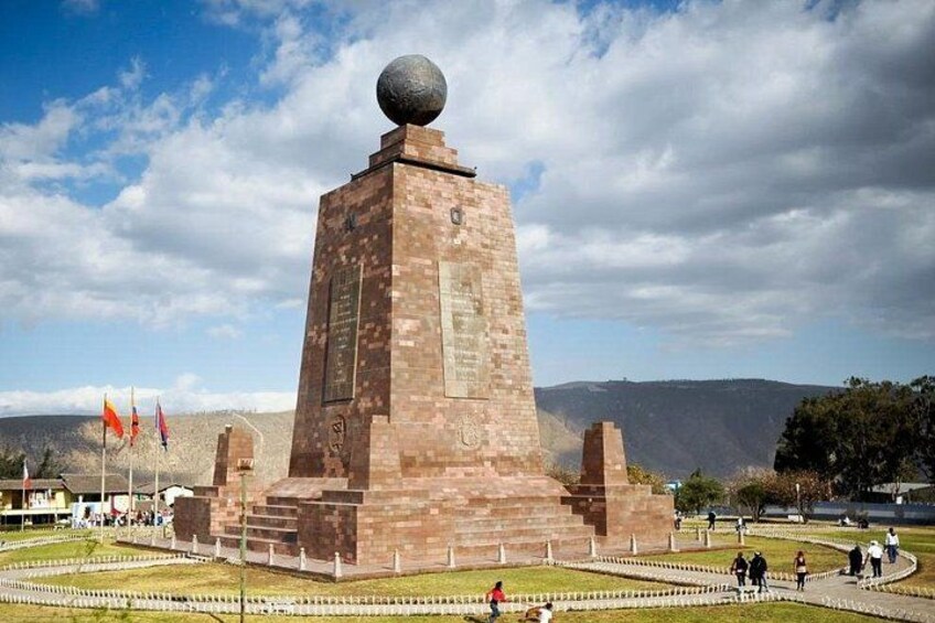 A tall brick monument with a spherical top, surrounded by a landscaped area with pathways and flags. 1
