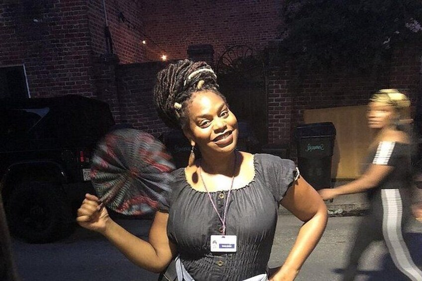 A person holding a fan, standing in an urban setting with brick buildings and a parked car. 2