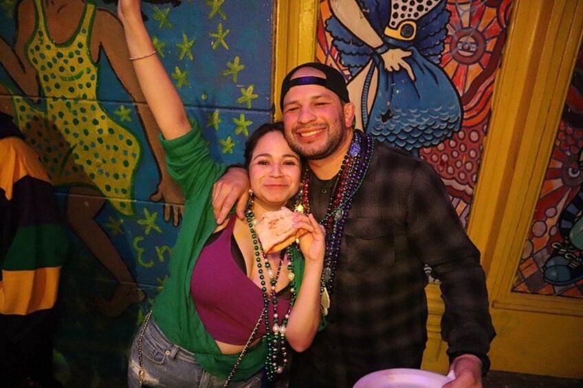 A person in a green top and denim shorts, a person in a plaid shirt, and a colorful mural in the background. 4