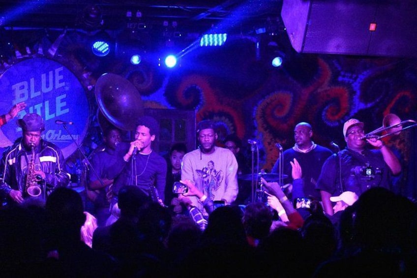 A band performing on stage with a large blue backdrop and a crowd in the foreground. 5