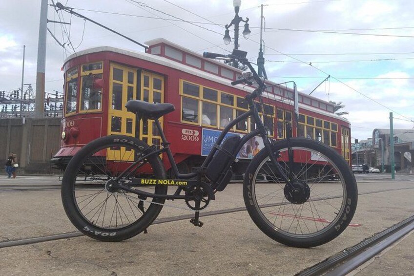 A red tram with yellow windows and a blue advertisement, a black bicycle with a basket, and tram tracks. 1