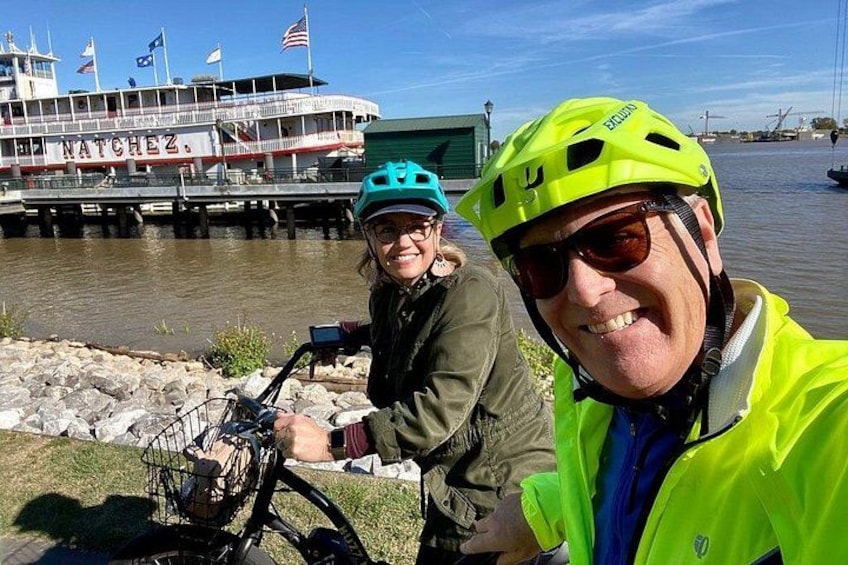 Two people wearing helmets and jackets by a dock with a boat named 'NATCHEZ' in the background. 4