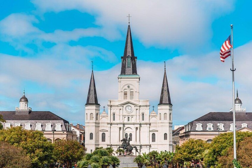 A historic church with two spires, a statue in front, and an American flag. 1